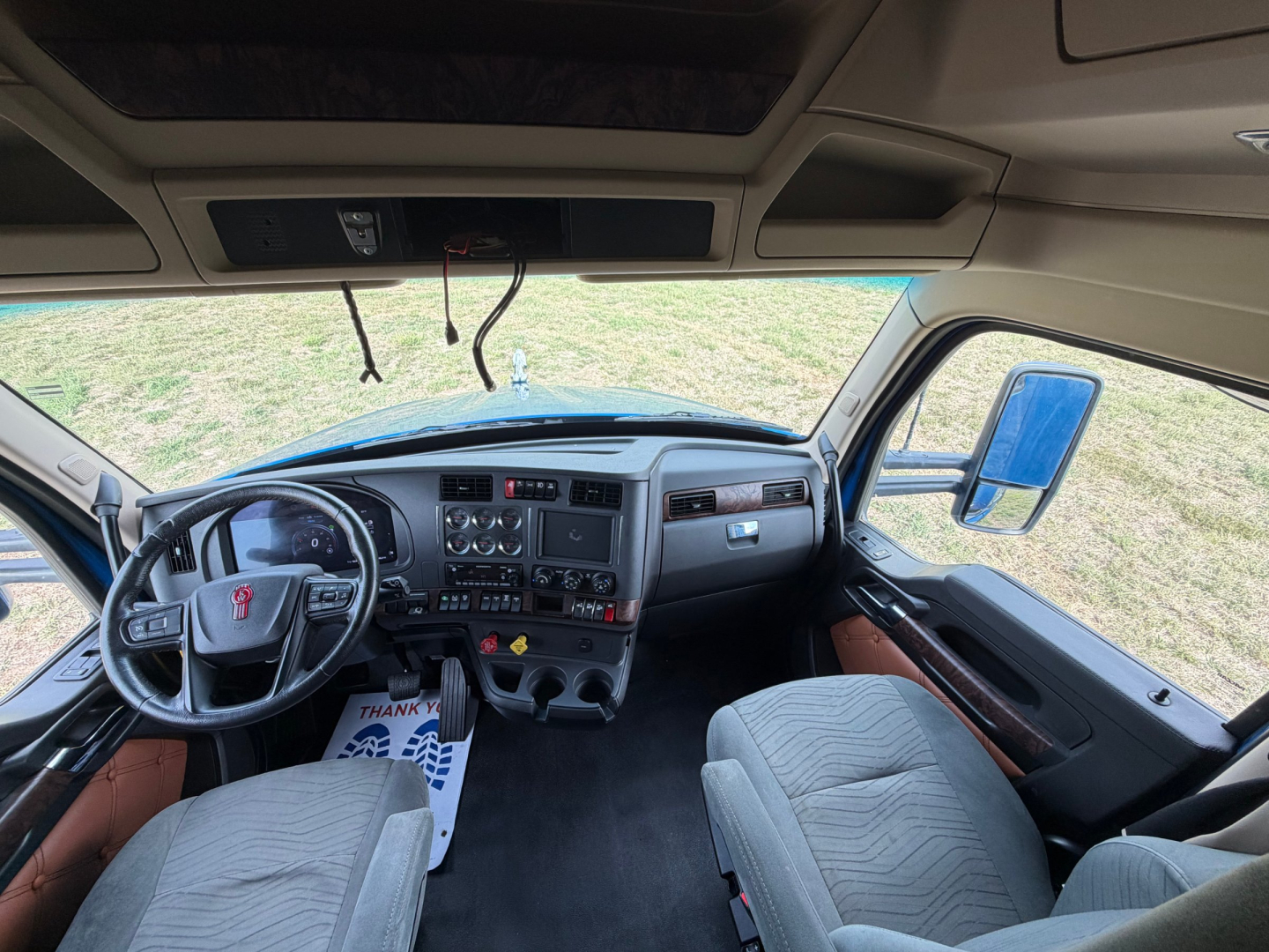 Kenworth T680 dashboard and steering wheel interior with grey fabric seats and overhead console, driver and passenger seats visible.