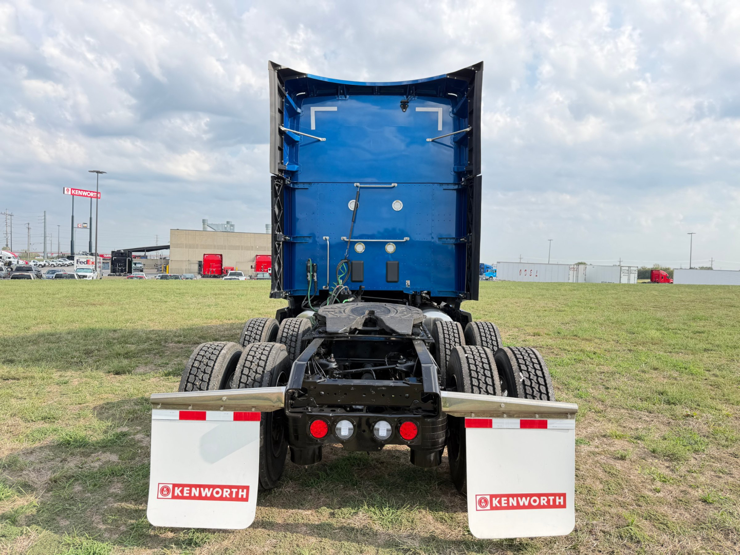 Kenworth truck chassis rear view showing blue dump bed, dual rear axles, mud flaps with Kenworth logos, and tail lights.