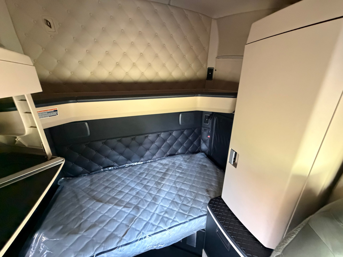 Kenworth T680 sleeper cab interior with quilted diamond-pattern upholstery on walls and bed, storage cabinet on the right, and side shelf.