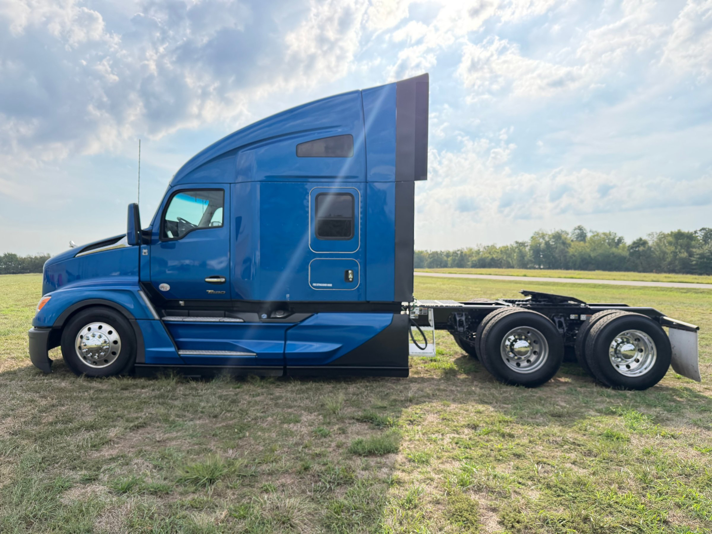 Kenworth T680 sleeper cab semi-truck in blue, side view showing cab and rear wheels.