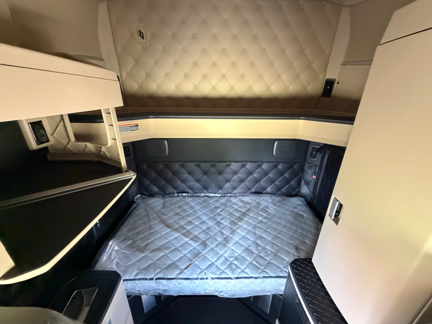 Kenworth truck sleeper interior showing quilted beige headliner and quilted gray bunk area with storage cabinets.