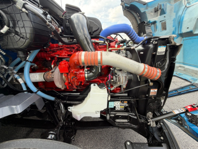 Kenworth T680 engine bay showing red engine block, blue hoses, large intake, and radiator area.