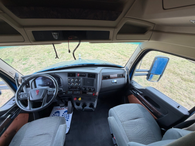Kenworth T680 dashboard and steering wheel interior with grey fabric seats and overhead console, driver and passenger seats visible.
