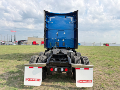 Kenworth truck chassis rear view showing blue dump bed, dual rear axles, mud flaps with Kenworth logos, and tail lights.