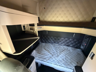 Kenworth T680 sleeper cab interior showing quilted headliner, upper bunk storage, and padded side panels with a gray quilted mattress in the sleeper area.