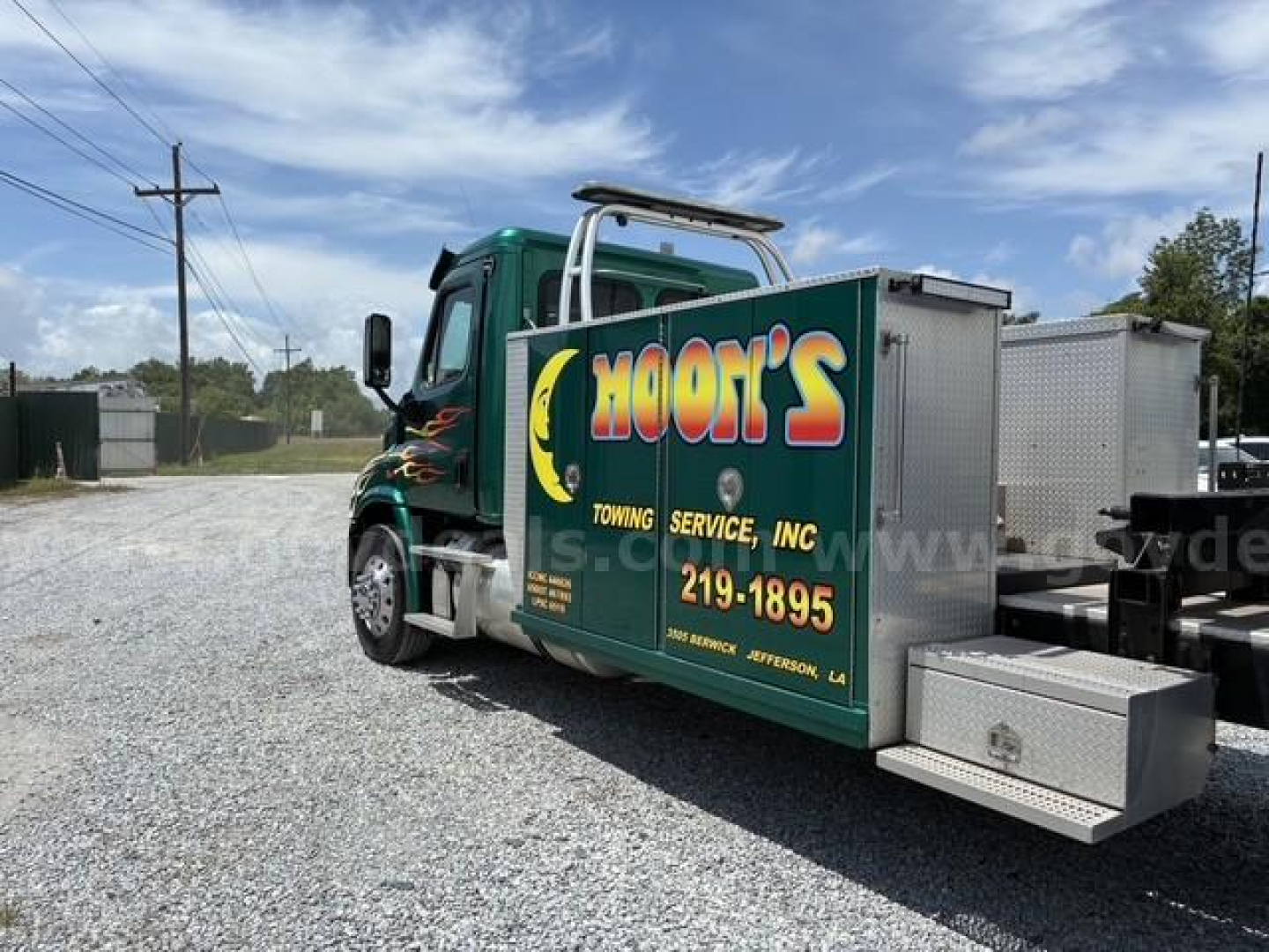 Truck cab with utility service box labeled MOON'S Towing Service Inc. showing green cab, graphic flames, aluminum toolbox, and towing equipment.