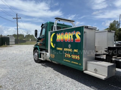 Truck cab with utility service box labeled MOON'S Towing Service Inc. showing green cab, graphic flames, aluminum toolbox, and towing equipment.