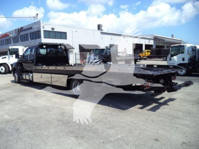 2017 Ford F650 rollback truck in a dealership lot showing a flatbed with towing equipment and extended cab.