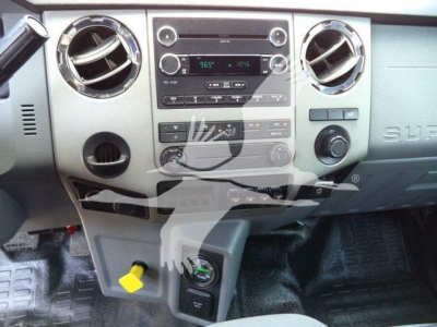 Ford F-650 dashboard center console showing stereo, climate controls, round air vents, and 12V/aux ports; steering column visible; yellow ignition switch cover.