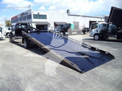 Ford F650 rollback truck with a long blue tilt-bed ramp in a dealership lot.
