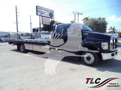 Ford F-Series cab and rollback bed with long chrome front, branding on door and wheel; TLC Truck Sales Center sign in background; VIN and stock visible in listing text overlay.