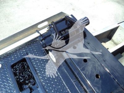 Trucks equipment bay with a winch motor and hydraulic control assembly mounted on a diamond-plate platform, visible bolts and cables.