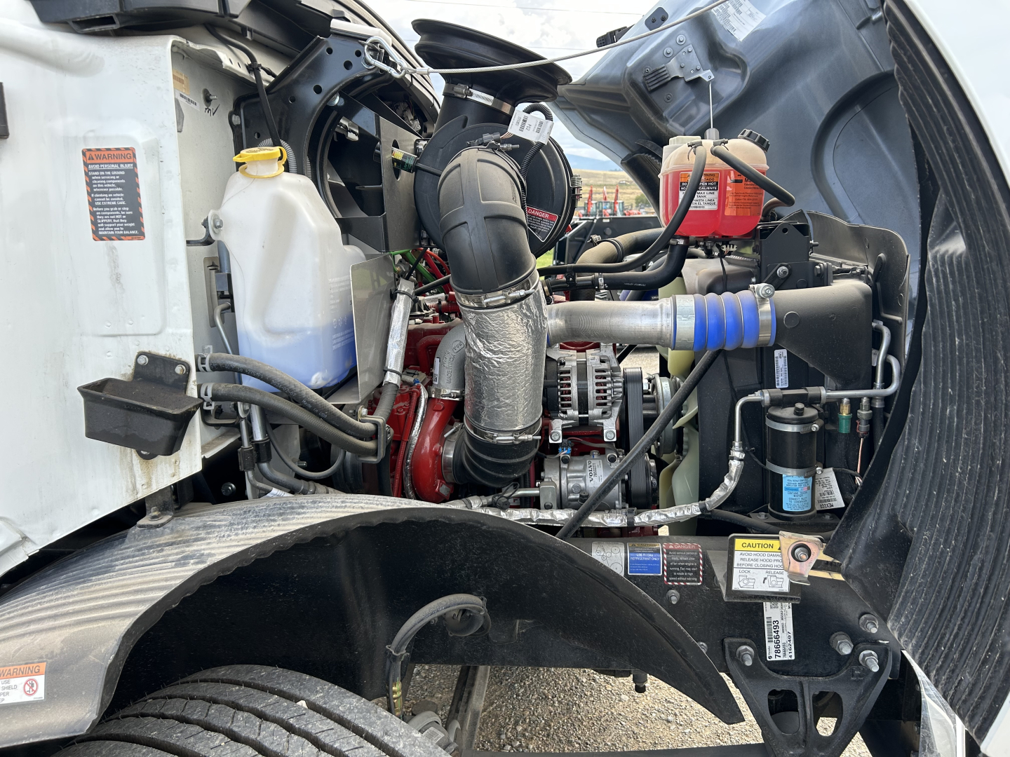 Mack MD7 engine bay showing coolant reservoir, air intake, hoses, and turbocharger with blue silicone coupler; various labels and a red coolant reservoir visible.