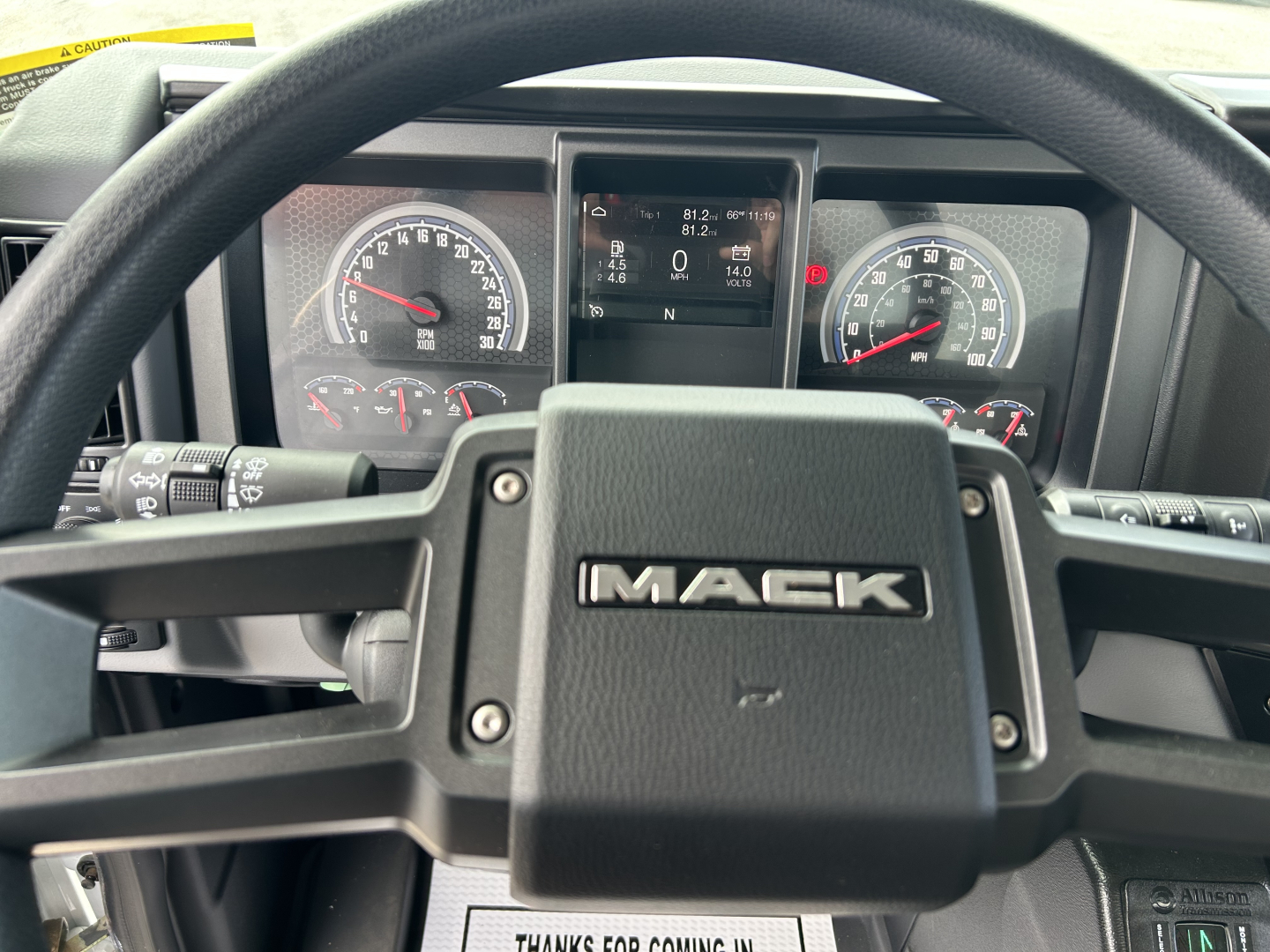 Mack MD7 steering wheel and instrument cluster view; dashboard displays gauges and center digital screen with vehicle info.