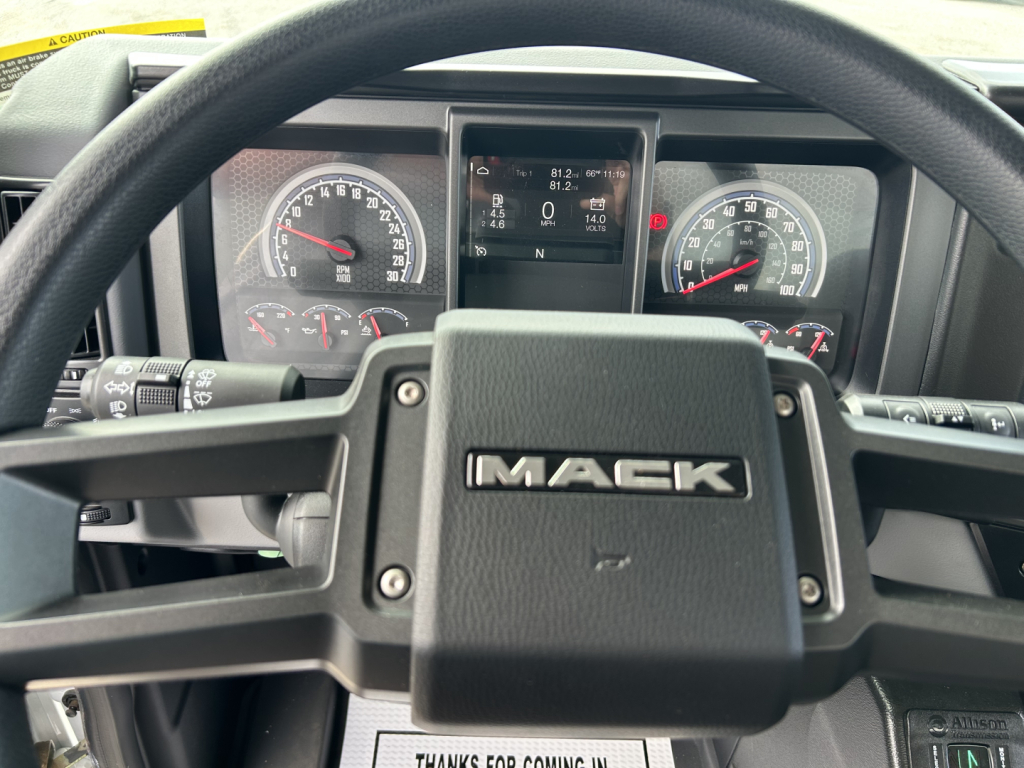 Mack MD7 steering wheel and instrument cluster view; dashboard displays gauges and center digital screen with vehicle info.