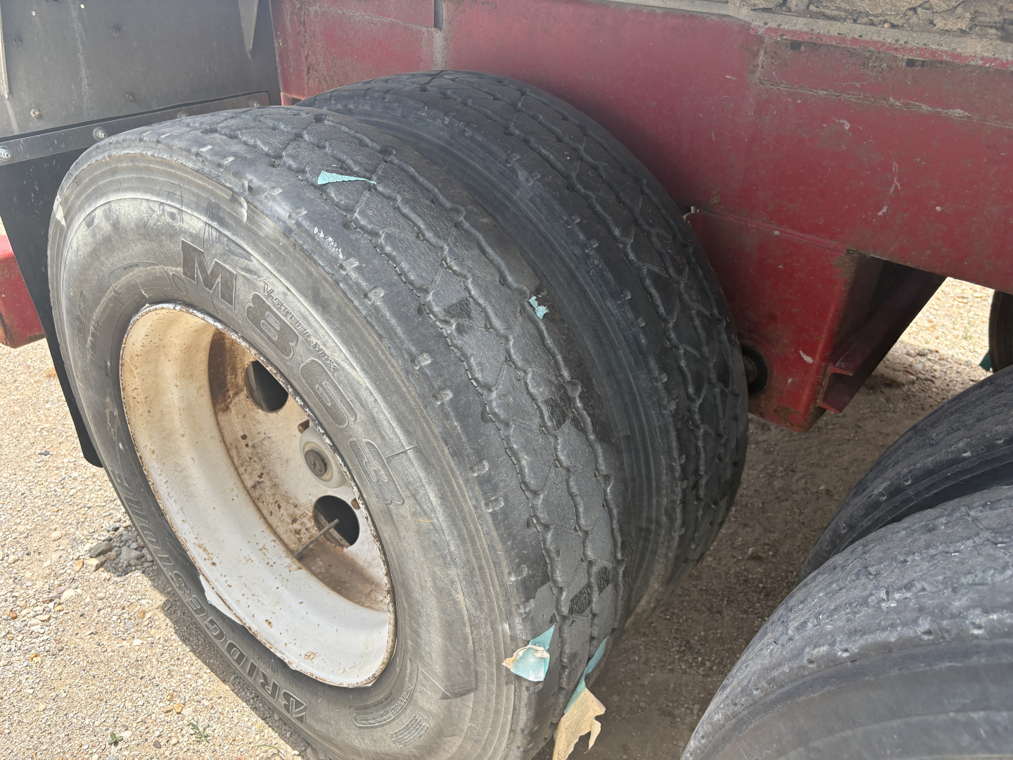 Trailer wheel showing worn dual tires and white rims on a red trailer, with visible tread wear and dirt.