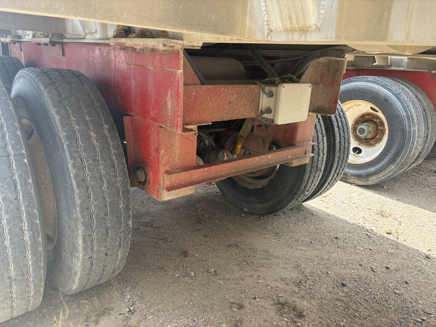 Trailer undercarriage showing dual rear axles and red steel frame with suspension components.