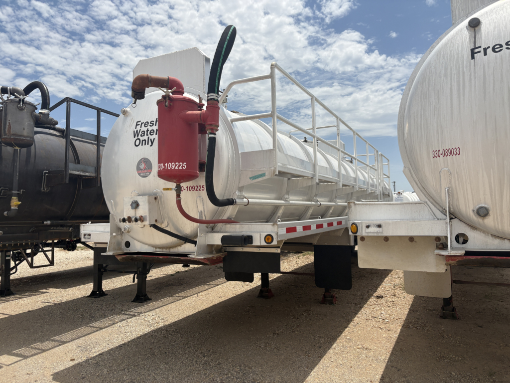 Trailer showing fresh water-only tank and red piping with white tanker and black undercarriage. Visible text includes Fresh Water Only and inspection numbers on the tank.