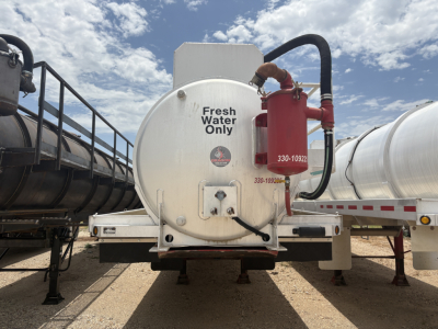 Vacuum trailer rear showing white cylindrical tank with Fresh Water Only label and red drain assembly mounted on the back.