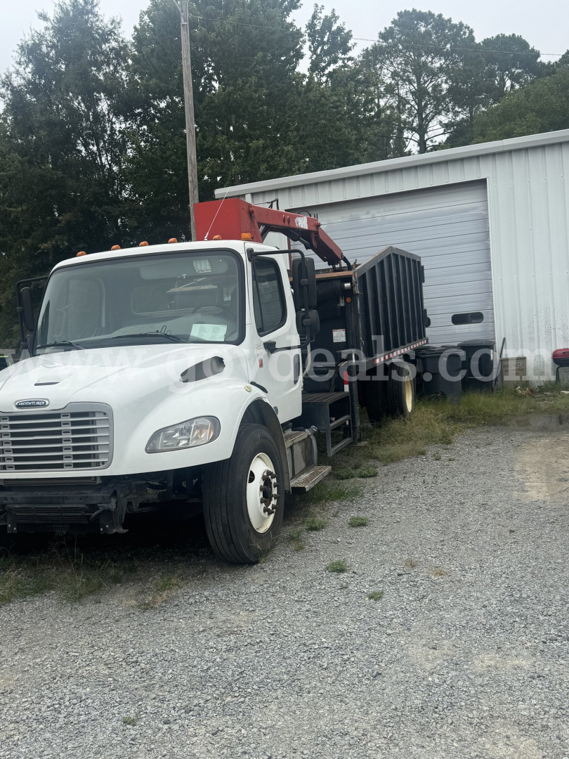 Forklift-mounted grapple on a Freightliner truck in a gravel lot with a white cab and red boom.