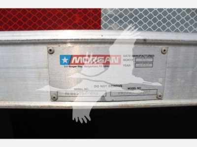 Gilded metal badge plate on truck rear showing Morgan logo and serial/model fields, faded text with 'Manufactured' label.