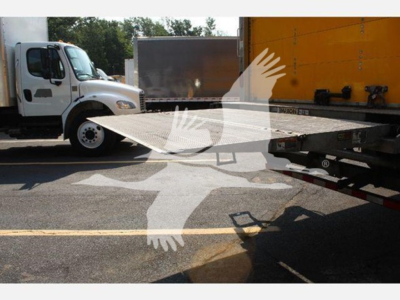 Truck scene showing a white freight truck with a flatbed trailer, part of a box truck behind, and a loading ramp visible.