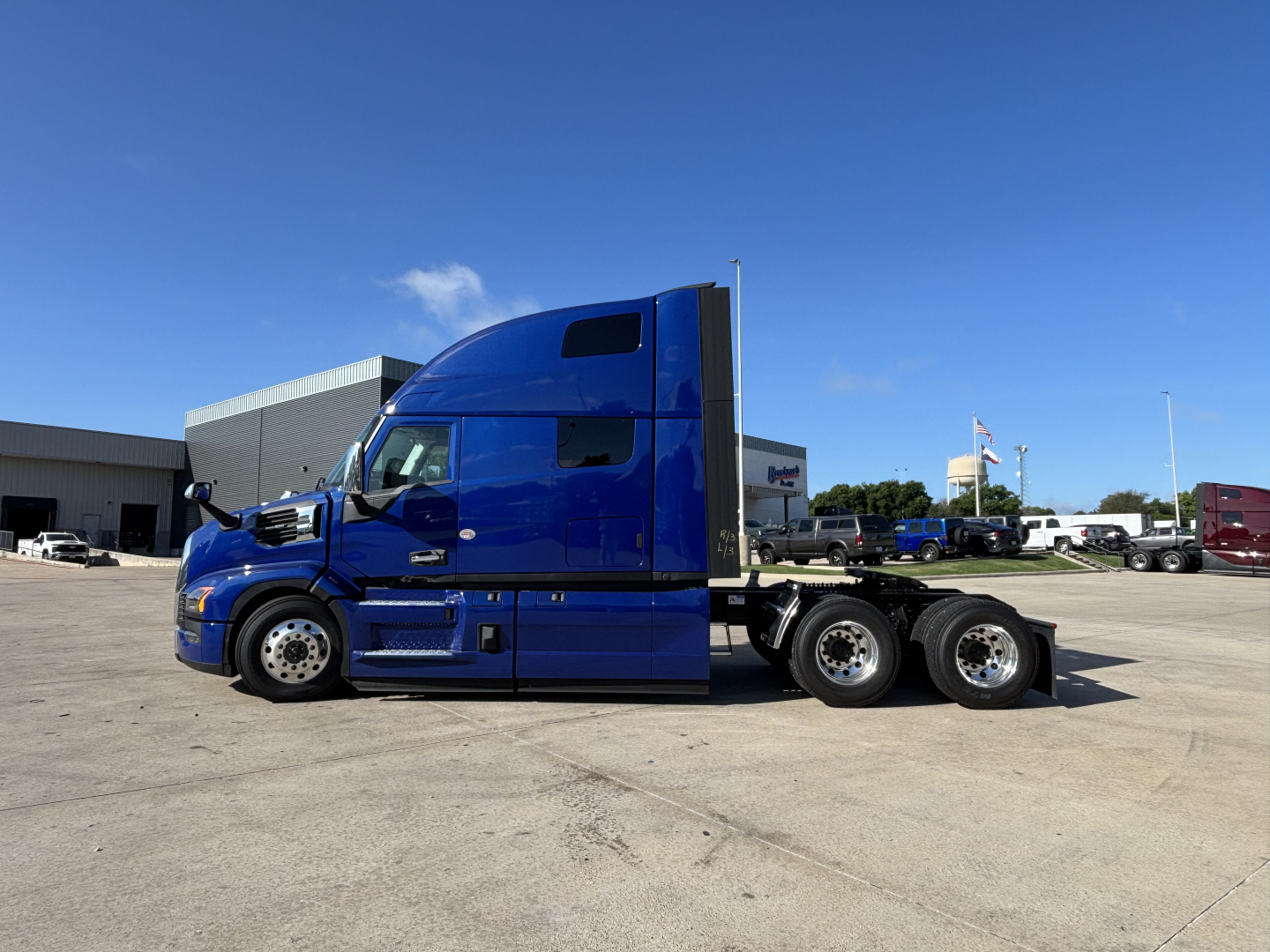 Blue Mack PR64T76H semi truck tractor side view with sleeper cab and triple rear axles in a parking lot.