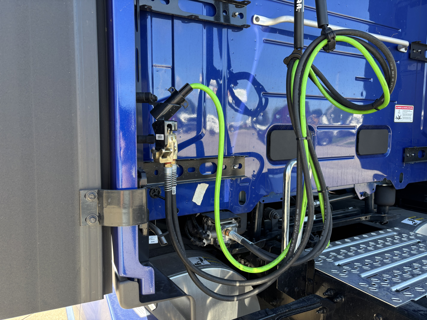 Trucks exterior show blue cab with bright green and black cables connected near door; metal stairs visible; side rails and mounting hardware.