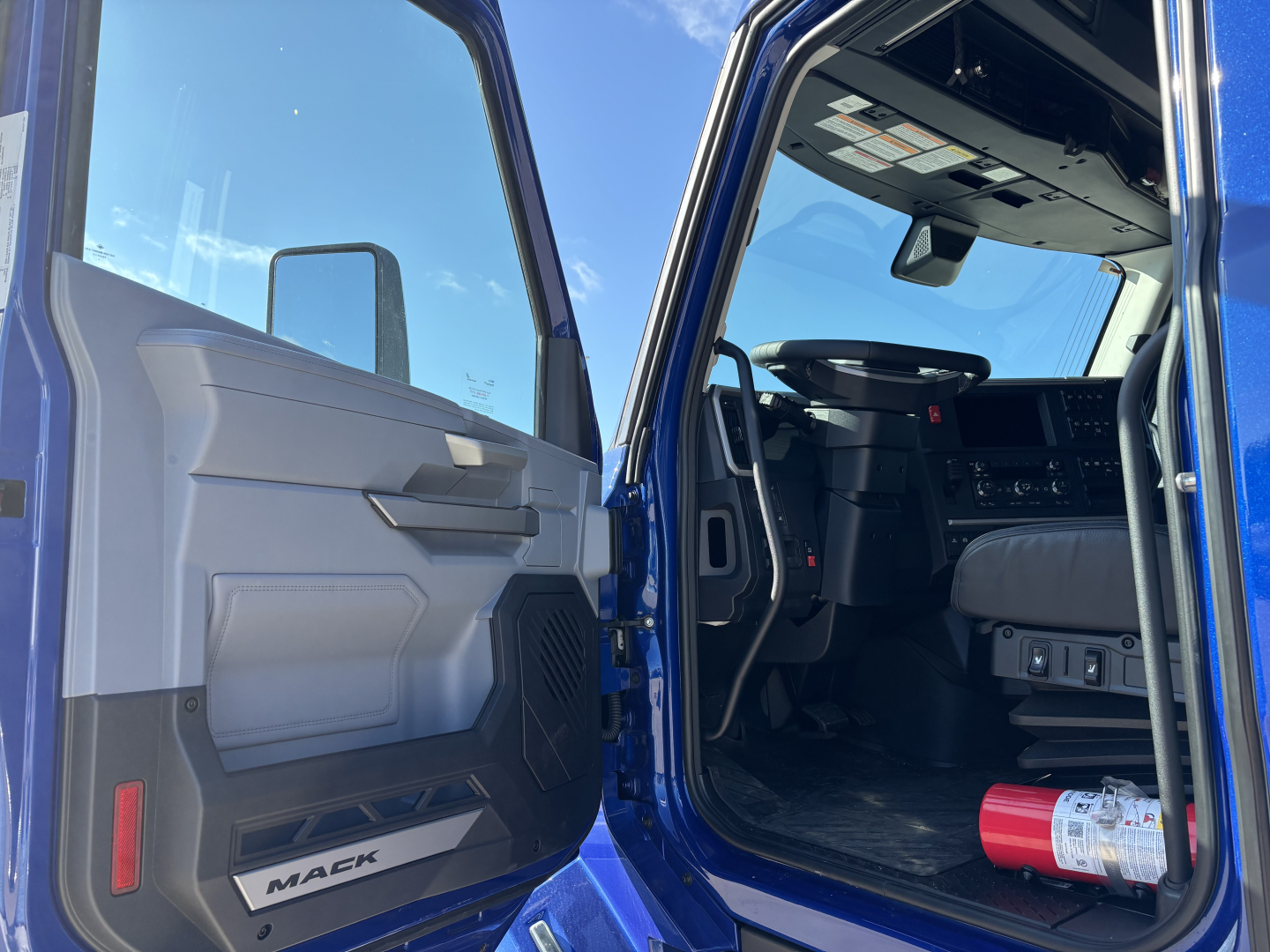 Mack PR64T76H tractor-trailer cab interior and open driver door showing dashboard and steering wheel.
