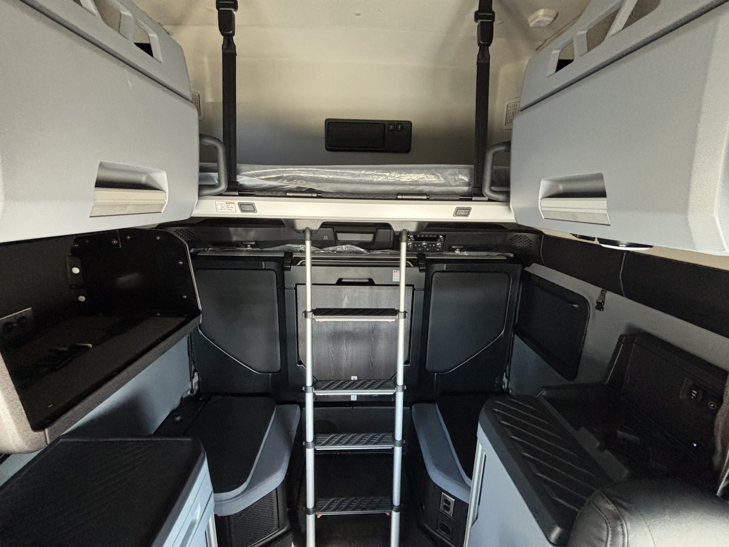 Cab interior of a new Mack PR64T76H truck showing sleeper bunk area with ladder and storage compartments.