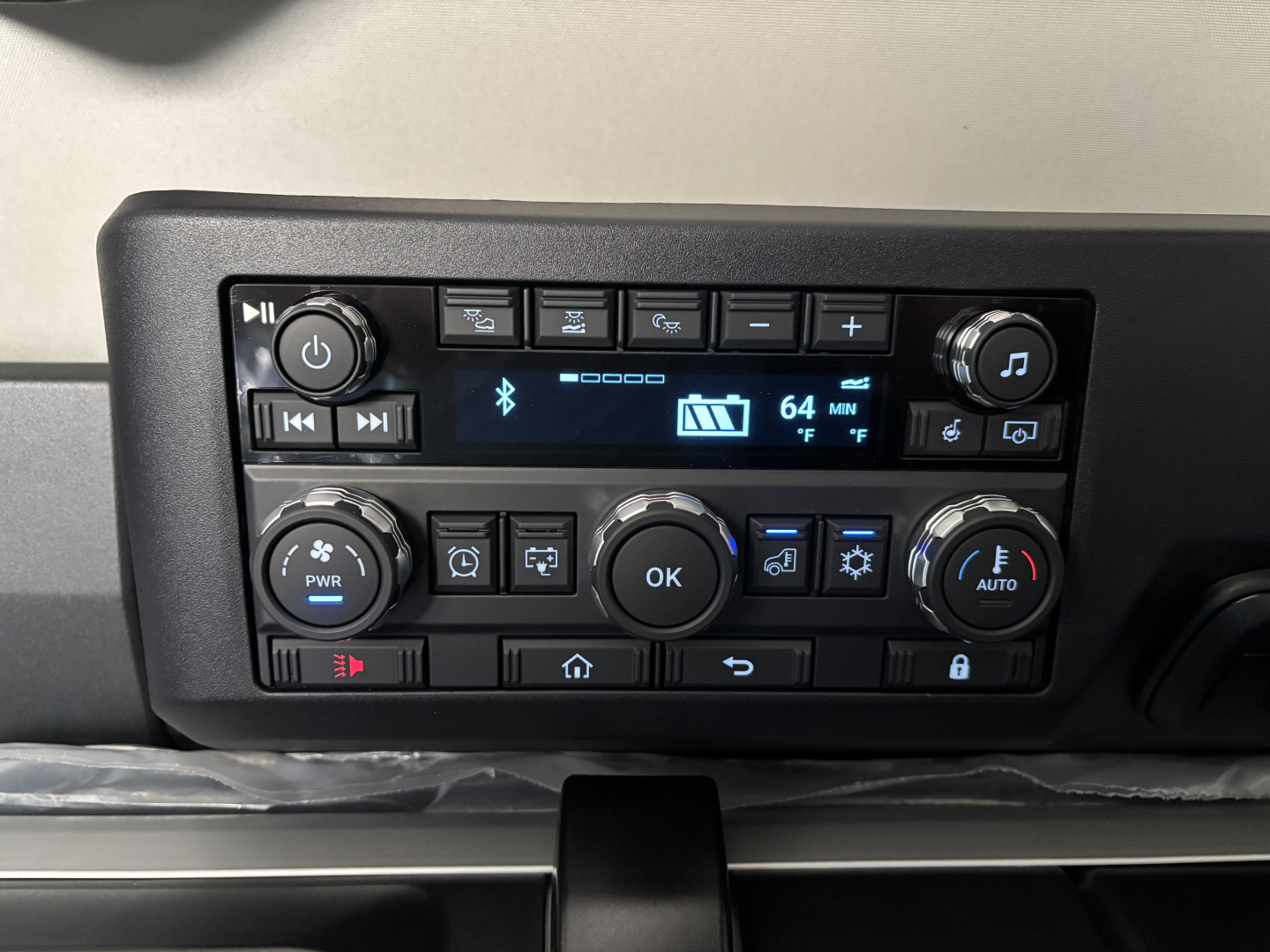Truck cab dashboard control panel showing climate controls, audio display, and multiple buttons; no text legible aside from digital readout.