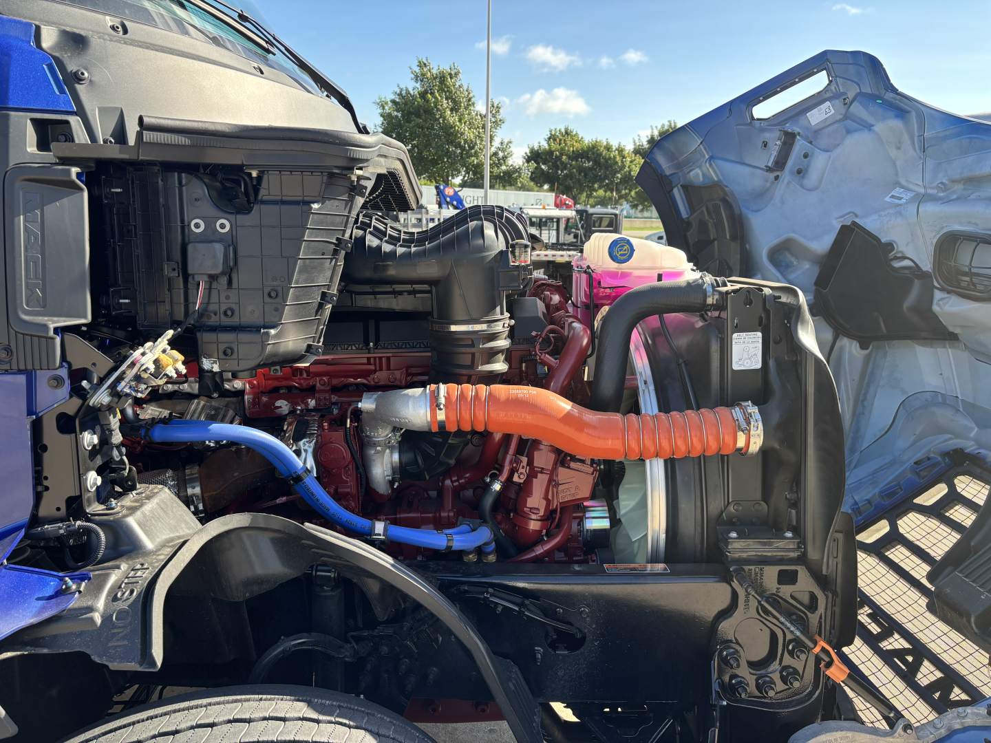 Mack PR64T76H engine bay showing orange turbo hose, blue coolant line, and red engine block components.