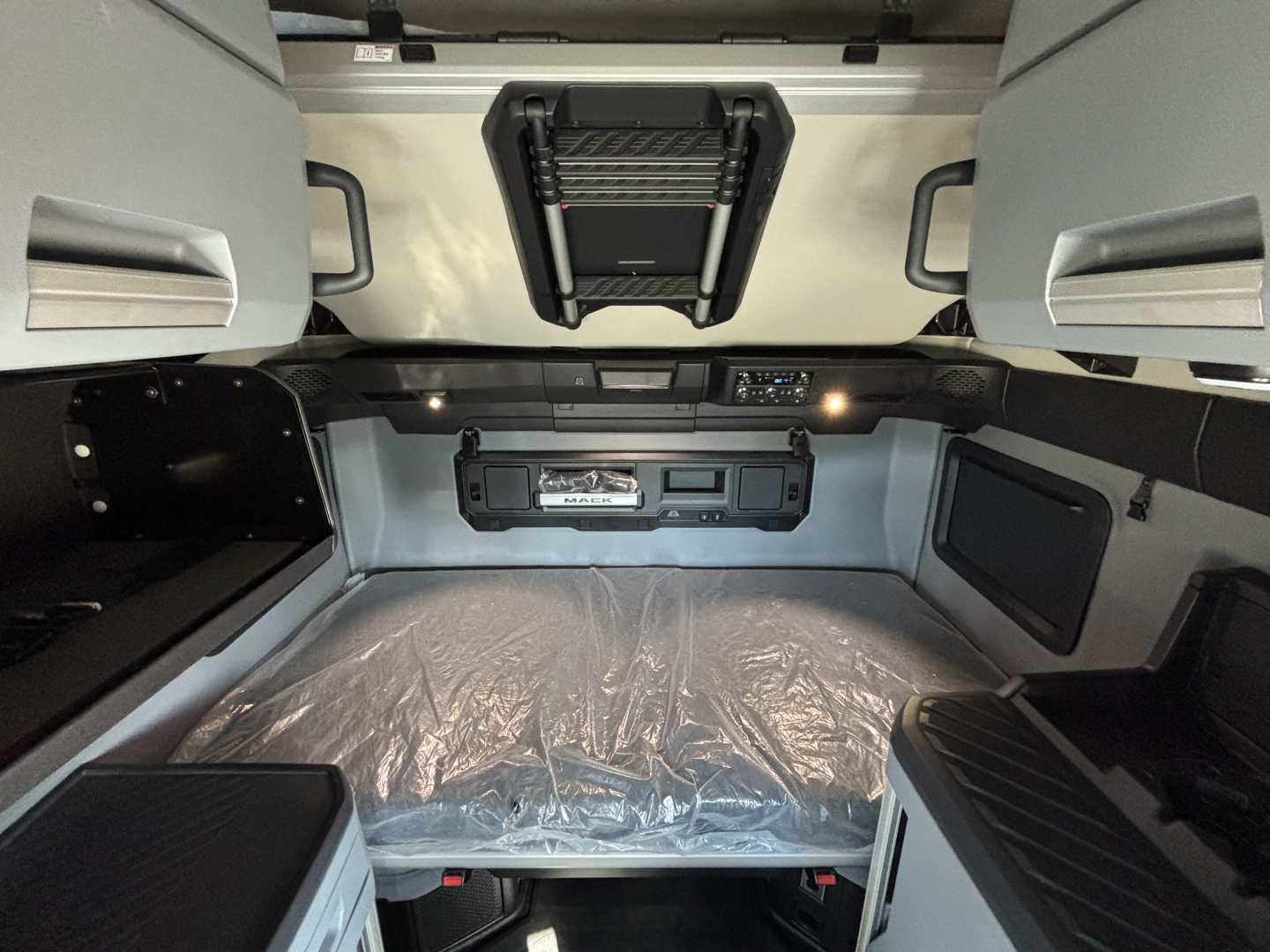 Truck cab interior with overhead sleeper bunk area and control panel; visible text includes a black label area on dash and a vent; no other legible text visible.