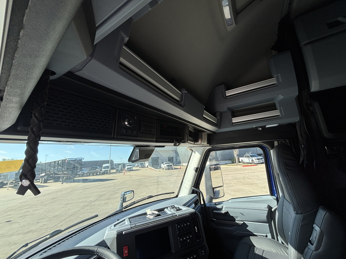 Cab interior of a 2027 Mack PR64T76H truck showing dashboard, overhead storage compartments, and driver seat from a forward-facing perspective.