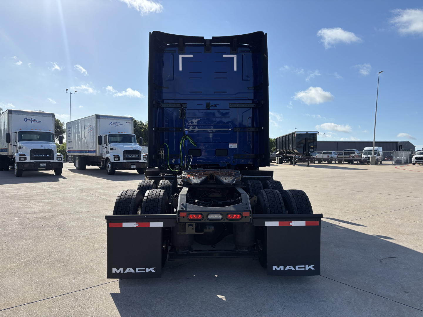 Mack PR64T76H truck chassis viewed from rear showing dual rear wheels and mud flaps with 'MACK' lettering in a dealership lot.