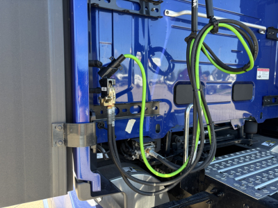 Trucks exterior show blue cab with bright green and black cables connected near door; metal stairs visible; side rails and mounting hardware.