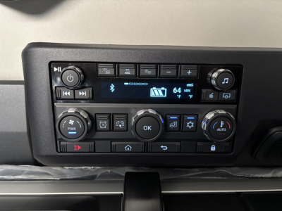 Truck cab dashboard control panel showing climate controls, audio display, and multiple buttons; no text legible aside from digital readout.