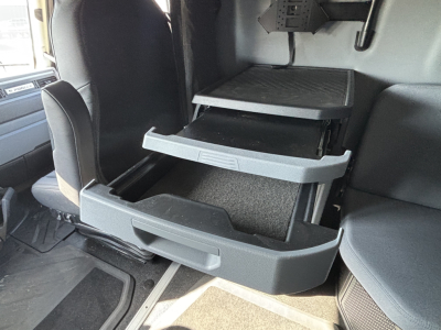 Truck cab interior showing a three-drawer under-seat storage system in the driver area of a Mack PR64T76H.
