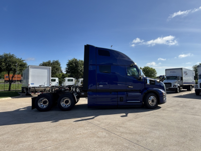 Tractor-trailer cab in blue side view showing bunk area and rear wheels with third axle in a truck lot.