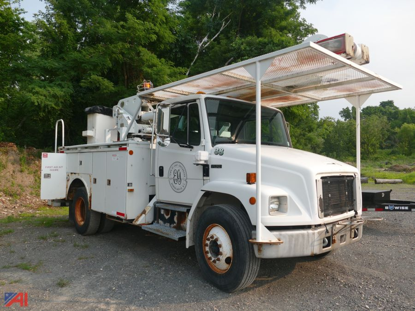Freightliner FL70 bucket truck side view showing service compartments, bucket winch, large white utility body, GE logo on door, and overhead platform; no specific model text readable.
