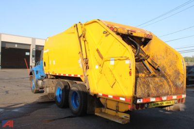 Side and rear view of a yellow New Way WorkStar 7400 refuse truck attached to a blue cab. Visible are the rear compactor, hydraulic arms, and dual rear wheels on multiple axles.