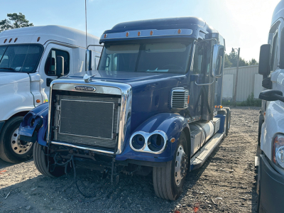 Conventional daycab truck front view showing large chrome radiator grille, dual round headlights, blue cab, and exposed front bumper; Freightliner Coronado styling.