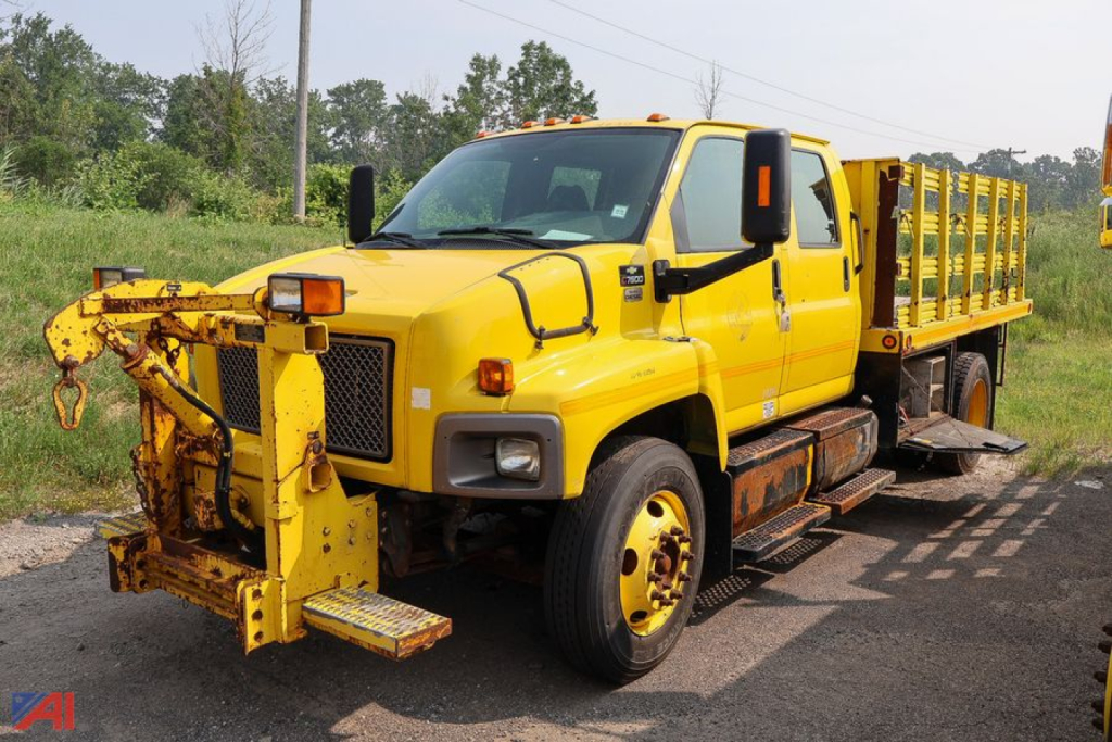 Chevrolet Kodiak C7500 crew cab stake truck with plow hitch in yellow, flatbed stake bed, dual rear wheels, exposed chassis and utility rack.