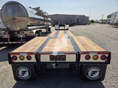 Flatbed trailer rear view with wooden deck and black mud flaps showing Fontaine Specialized branding. Dual tires, red and amber lights, metal frame, and steel hitch visible.