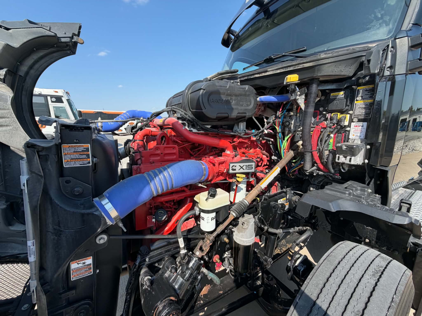 Kenworth T680 engine bay showing red labeled engine components, blue hose, and various wiring in front of cab.
