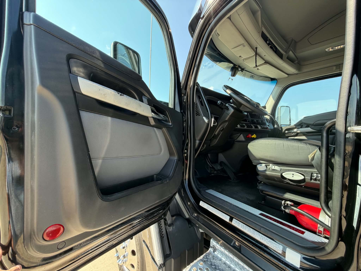 Kenworth T680 cab interior and open driver door showing dashboard and seat area.