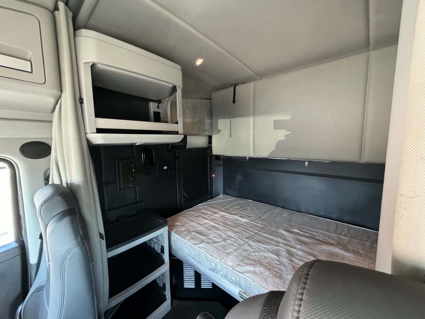 Interior sleeper cab of a Kenworth T680 showing a bed with mattress, overhead cabinets, and storage compartments in a cab area.