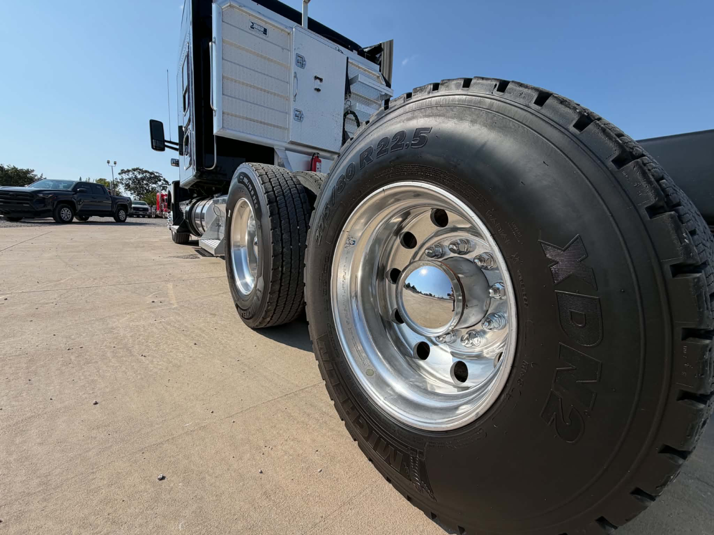 Kenworth T680 truck wheel and dual rear tires with polished hubcap and rugged tire tread; side cab area visible in background.