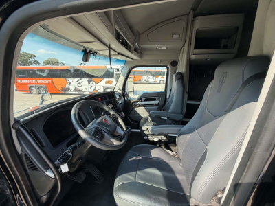 Kenworth T680 cab interior with steering wheel, driver and passenger seats, and dashboard visible through open driver door.