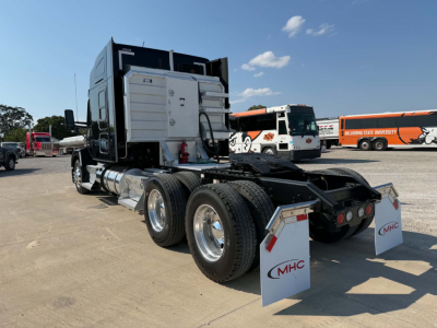Kenworth T680 tractor rear/side view showing dual rear axles, chrome fuel tanks, and white rear mud flaps with MHC logos. No detailed labeling visible on components.